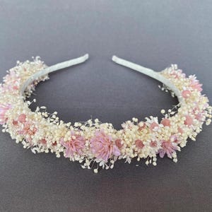 May include: A delicate headband adorned with a circle of white and pink dried flowers. The headband is made of a thin, flexible wire and is perfect for adding a touch of elegance to any hairstyle.