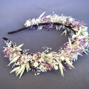 May include: A delicate floral headband with dried white and purple flowers and grasses. The headband is made of a black elastic band.