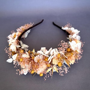 May include: A delicate headband adorned with dried flowers in shades of white, pink, and gold. The headband features a variety of dried flowers, including hydrangeas, baby's breath, and dried berries.