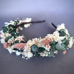 May include: A white and pink floral headband with eucalyptus leaves. The headband is made with dried flowers and is perfect for a wedding or special occasion.