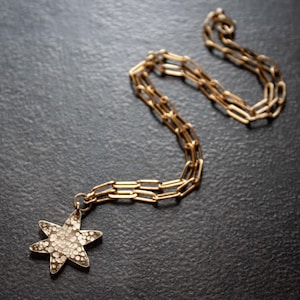 May include: Gold-toned necklace with a starfish pendant. The pendant is encrusted with small, sparkling stones. The chain is a linked design, and the necklace is displayed on a dark, textured surface.