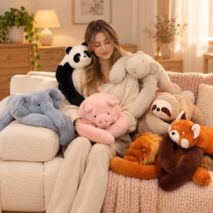 May include: A collection of plush stuffed animals including a black and white panda, a light grey elephant, a pink pig, a beige sloth, a golden-brown lion, and a red panda with dark brown limbs, all featuring soft, textured fabric surfaces.