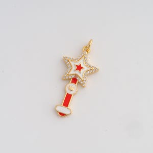 May include: A gold-colored star-shaped pendant with a red and white design. The star is encrusted with small, clear crystals. The pendant has a red and white handle with a small crown detail.