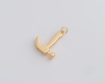 May include: A gold-colored hammer pendant with a small loop at the top for attaching to a chain or bracelet. The hammer has a curved claw and a flat striking face. The pendant is likely made of metal and is set against a white background.