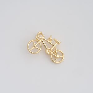 May include: A gold-colored bicycle charm with a detailed design. The bicycle has a classic frame, wheels with spokes, a seat, and handlebars. The charm is likely made of metal and is suitable for jewelry making or as a decorative element.