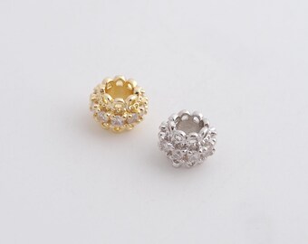 May include: Two round jewelry beads, one in gold tone and one in silver tone, each featuring a central band of clear, faceted stones set within a decorative, scalloped metal frame with a hollow center for threading onto a cord or chain.