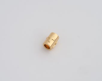 Op de afbeelding: Een kleine, cilindrische goudkleurige kraal met een hol midden. De kraal heeft een geometrisch ontwerp met een kruisvorm aan de buitenkant. De kraal is ongeveer 1,3 cm lang en staat tegen een witte achtergrond.