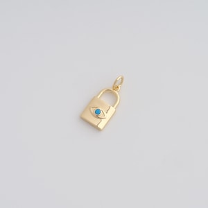 May include: A gold-colored padlock charm with a turquoise eye design. The charm has a rectangular body with a curved handle and a small loop for attaching to a necklace or bracelet. The eye is centered on the padlock.
