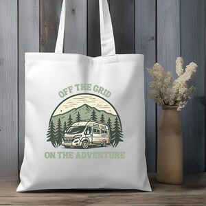 Könnte beinhalten: Weiße Canvas-Tragetasche mit einer grünen, braunen und weißen Illustration eines Wohnmobils in einer Berglandschaft. Der Text "Off the Grid On the Adventure" ist auf die Tasche gedruckt.