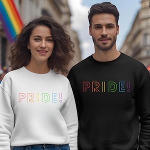 Peut inclure: Deux sweatshirts, un blanc et un noir, avec le mot "PRIDE!" en lettres arc-en-ciel. Les sweats sont de style col rond. L'arrière-plan montre une scène de rue avec un drapeau arc-en-ciel.
