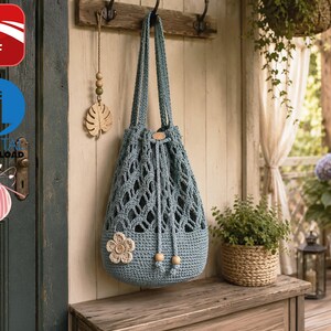May include: A dusty blue crochet drawstring bag featuring an openwork diamond pattern on the upper section, a solid base, and a single cream-colored crocheted flower embellishment. The bag includes two long shoulder straps and wooden bead accents.