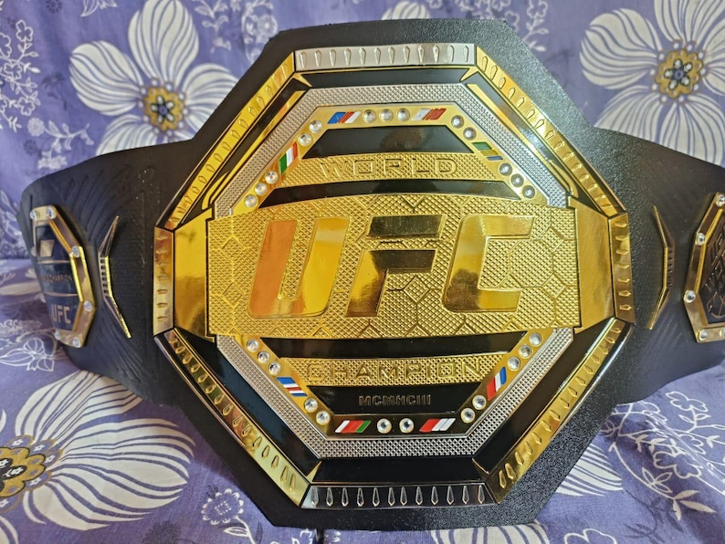 May include: A black leather UFC championship belt with a gold octagon-shaped plate featuring the UFC logo and the words "World Champion".