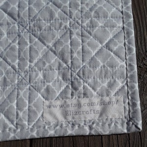 Pu&ograve; includere: Primo piano di un tessuto trapuntato grigio con un motivo geometrico bianco. Il tessuto &egrave; cucito a rombi. Un'etichetta con il testo "www.etsy.com/shop/ Elizcrafts" &egrave; cucita sul tessuto.
