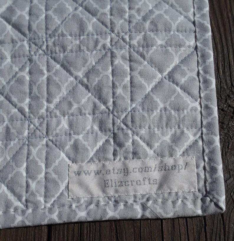 Pu&ograve; includere: Primo piano di un tessuto trapuntato grigio con un motivo geometrico bianco. Il tessuto &egrave; cucito a rombi. Un'etichetta con il testo "www.etsy.com/shop/ Elizcrafts" &egrave; cucita sul tessuto.