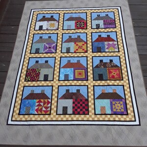 May include: A quilt with a patchwork design featuring 12 houses with different coloured roofs and windows. Each house has a unique pattern on the front.