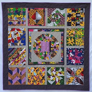 May include: A quilt with a patchwork design featuring various geometric shapes and patterns in shades of purple, green, yellow, red, and blue. The quilt is made up of 12 individual squares, each with a unique design.