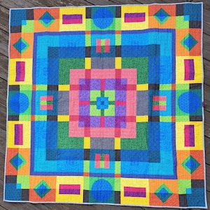May include: A colorful quilt with a geometric pattern of squares, diamonds, and circles in shades of blue, green, red, yellow, and purple.