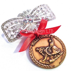 May include: A silver rhinestone bow brooch with a red ribbon attached to a bronze medal with the words "Molly Pitcher" and a depiction of a woman loading a cannon.