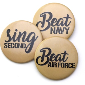 May include: Three round, tan-colored buttons with black text. The first button says "Sing Second". The second button says "Beat Navy". The third button says "Beat Air Force".