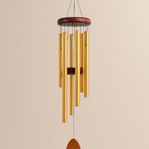 May include: A wind chime with gold-colored metal tubes suspended from a dark brown wooden disc. A smaller wooden piece is centered below the tubes. The wind chime hangs from a black string.