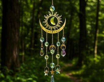 May include: A gold-colored suncatcher with a sun and crescent moon design, adorned with hanging crystal beads and stars. The sun and moon feature a green crystal center. The suncatcher is suspended by a chain, creating a decorative and celestial-themed ornament.