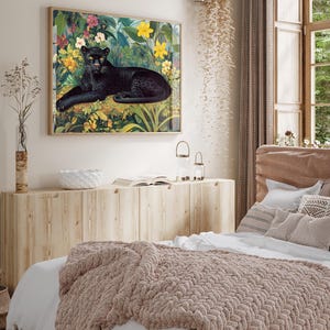 Op de afbeelding: Een ingelijste kunstdruk met een zwarte panter die rust te midden van weelderig groen en kleurrijke bloemen. Het kunstwerk, met zijn houten lijst, toont een gedetailleerde illustratie van de panter en zijn omgeving. De print is in vintage stijl.