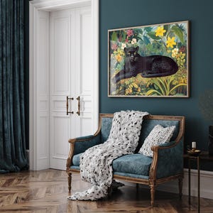 Op de afbeelding: Een ingelijste kunstdruk met een zwarte panter die rust in een weelderige, kleurrijke junglesc&egrave;ne met gele en roze bloemen. Het kunstwerk hangt boven een blauwgroene bank met een decoratief kleed en kussen.