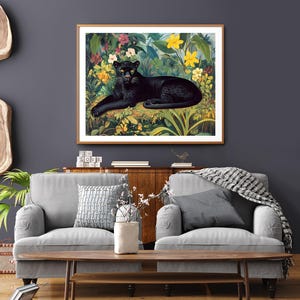 Op de afbeelding: Een ingelijste kunstdruk met een zwarte panter die rust in een weelderige, kleurrijke jungle. Het kunstwerk toont de panter met gele ogen, omringd door levendige bloemen en bladeren, in een houten lijst.