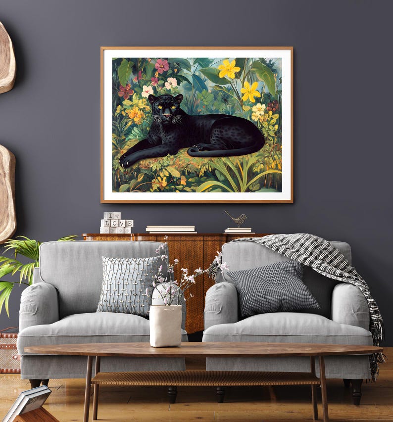Op de afbeelding: Een ingelijste kunstdruk met een zwarte panter die rust in een weelderige, kleurrijke jungle. Het kunstwerk toont de panter met gele ogen, omringd door levendige bloemen en bladeren, in een houten lijst.