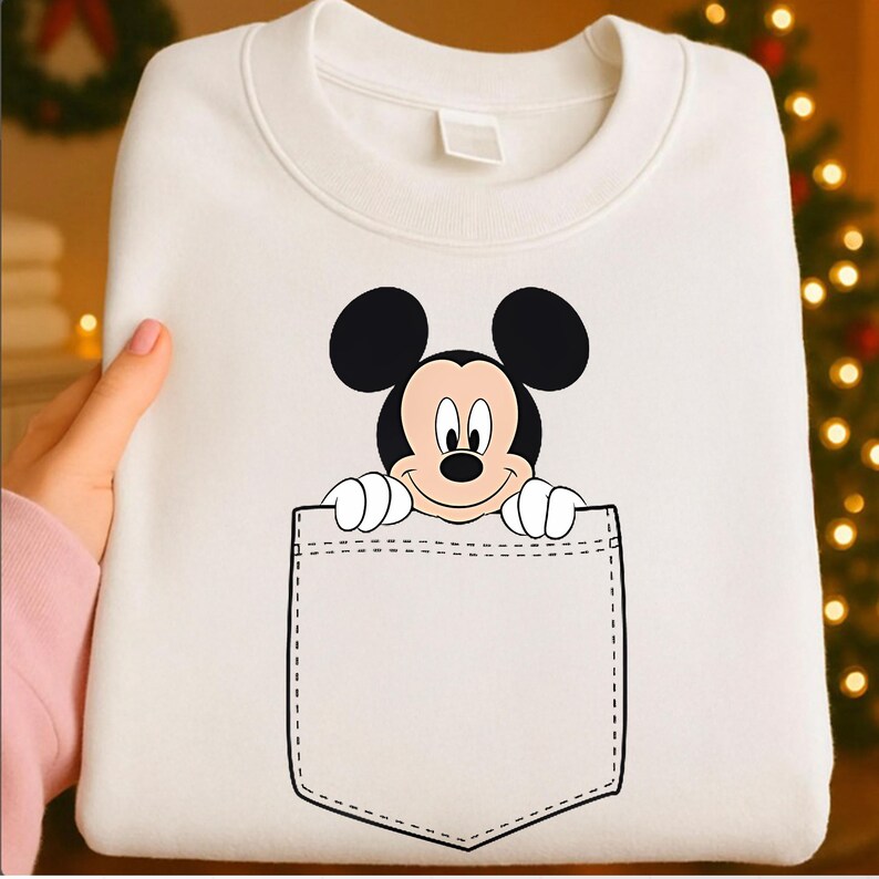 May include: White sweatshirt featuring a graphic of Mickey Mouse peeking out of a pocket. The Mickey Mouse graphic is in black, red, and white. The pocket is outlined in black stitching.