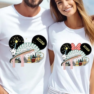 May include: White t-shirts with a colorful graphic featuring a stylized Spaceship Earth, a wand, and the year 2026. One shirt has a red polka dot bow, the other has a star. The design is in the style of Mickey Mouse ears.