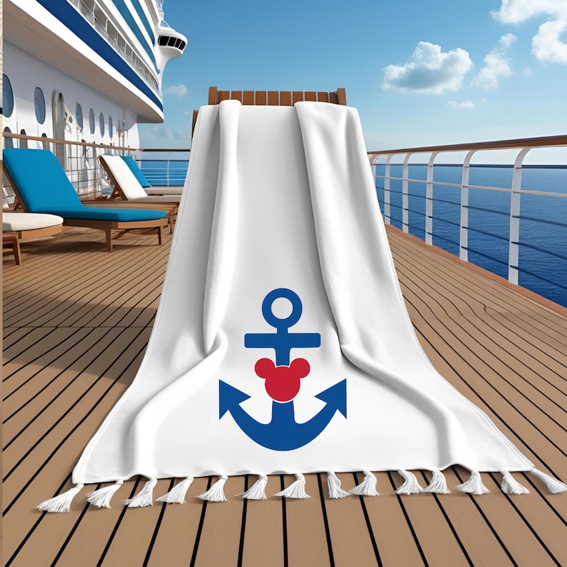 May include: White beach towel with a blue anchor design and a red Mickey Mouse head in the center. The towel has white tassels along the bottom edge. The towel is draped over a wooden chair on a cruise ship deck.
