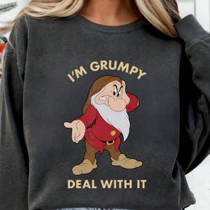 Puede incluir: Sudadera gris oscuro con una imagen de dibujos animados de Gruñón de Blancanieves. El personaje lleva un abrigo rojo y pantalones marrones, con el texto "I'M GRUMPY DEAL WITH IT" en blanco.