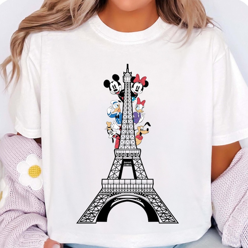 May include: White t-shirt with a black and white illustration of Mickey Mouse, Minnie Mouse, Donald Duck, Goofy, and Pluto standing in front of the Eiffel Tower.