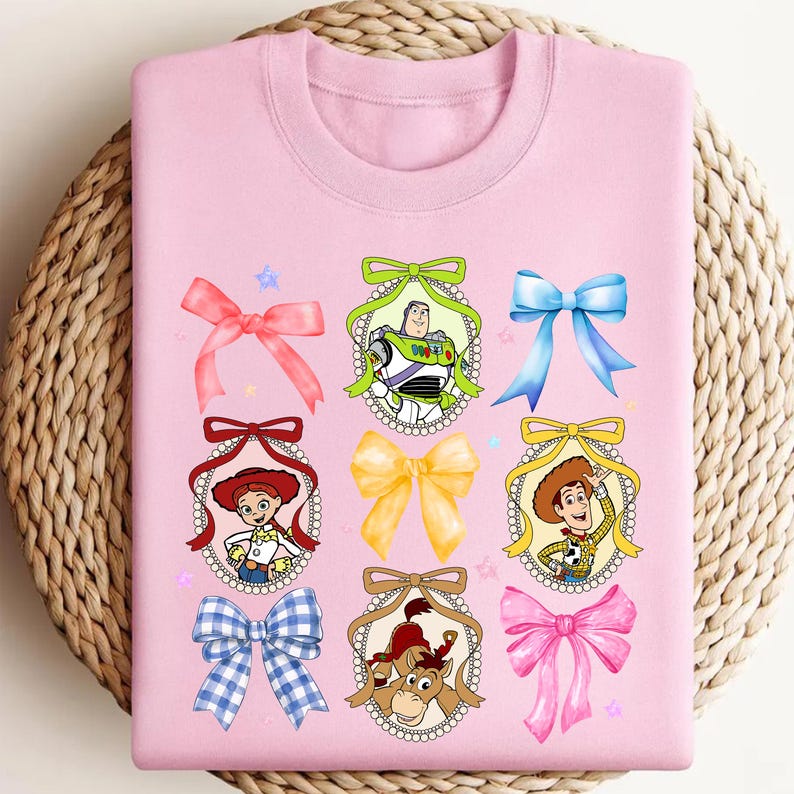 Puede incluir: Sudadera rosa claro con cuello redondo con retratos de personajes de dibujos animados dentro de marcos decorativos y lazos coloridos. Los personajes incluyen a Buzz Lightyear, Woody y Jessie. Un dise&ntilde;o l&uacute;dico para los fan&aacute;ticos de la pel&iacute;cula animada.