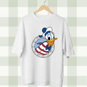 May include: White t-shirt featuring a cartoon image of Donald Duck peeking through a porthole. Donald Duck is wearing a sailor hat and bow tie. The porthole has a red and white striped design.