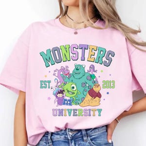 Puede incluir: Camiseta rosa con un gr&aacute;fico colorido de personajes de la Universidad de Monstruos. El gr&aacute;fico incluye el texto "Monsters University" y "Est. 2013".