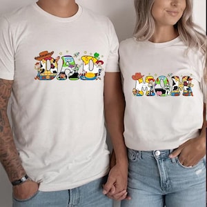 May include: Two white t-shirts with a Toy Story theme. The shirt on the left says "DAD" with the letters made up of Toy Story characters. The shirt on the right says "MOM" with the letters made up of Toy Story characters.