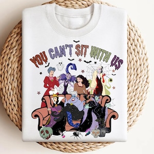 May include: White sweatshirt featuring a colorful graphic of Disney villains seated on a couch. The phrase "YOU CAN'T SIT WITH US" is printed above the characters. The design includes bats, stars, and a spiderweb.