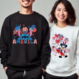 May include: Black sweatshirt featuring a blue Stitch character wearing a patriotic hat, with the word "AMERICA" in red, white, and blue. The design includes American flags and stars. A white sweatshirt features Mickey Mouse in a patriotic outfit.