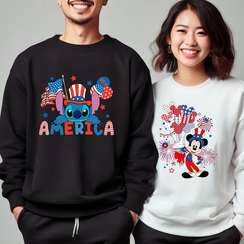 May include: Black sweatshirt featuring a blue Stitch character wearing a patriotic hat, with the word "AMERICA" in red, white, and blue. The design includes American flags and stars. A white sweatshirt features Mickey Mouse in a patriotic outfit.