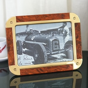 May include: A rectangular picture frame featuring a polished brass border with rounded corners and a rich burl wood inlay. The frame holds a black and white photograph of a vintage race car with the number six and a driver waving from the cockpit.