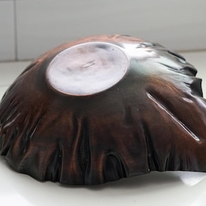 Puede incluir: Un cuenco de madera marr&oacute;n oscuro hecho a mano con una forma org&aacute;nica &uacute;nica. El cuenco tiene un interior liso y pulido y un exterior texturizado, que muestra la veta natural de la madera. El dise&ntilde;o del cuenco recuerda a una forma natural.