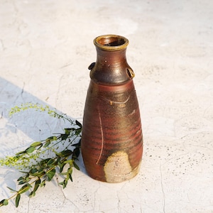 May include: A handmade ceramic vase with a brown and reddish-brown glaze. The vase has a narrow neck, a wide body, and two small handles. The vase is approximately 20 cm tall and has a unique, rustic appearance.