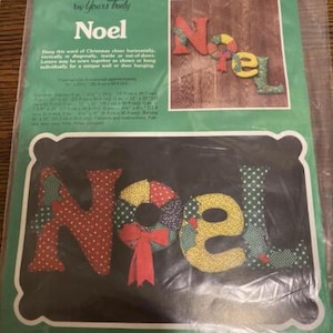 May include: A patchwork kit to create a "Noel" sign. The kit includes fabric pieces in red, green, white, and yellow with polka dots and floral patterns. The finished sign is approximately 12 inches wide and 4 inches tall.