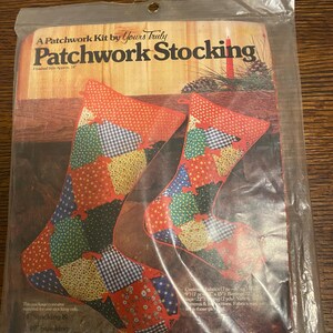 May include: A patchwork kit for making a Christmas stocking. The kit includes fabric pieces in red, green, blue, and white with various patterns. The finished stocking will be approximately 14 inches long.