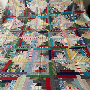 May include: A colorful patchwork quilt with a log cabin pattern. The quilt is made of various fabrics in shades of red, blue, green, yellow, and white. The quilt is laid out on a white bed frame.