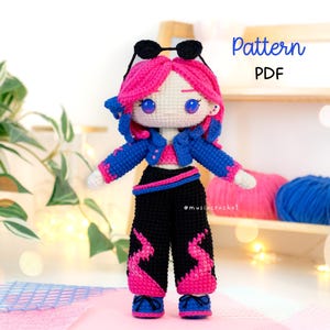 May include: A crochet doll with bright pink hair, wearing black sunglasses on its head, a blue cropped jacket, a pink top, and black trousers with pink flame-like patterns. The doll has large blue eyes and wears blue shoes. Text reads Pattern PDF.