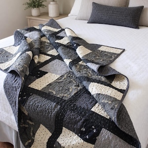 May include: A patchwork quilt featuring a monochromatic color scheme of black, white, and various shades of gray. The fabric squares display diverse patterns, including small dots, floral motifs, and intricate swirling quilted stitching.