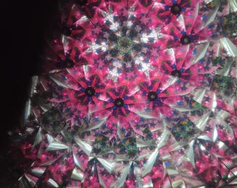 May include: Abstract image of a kaleidoscope's interior, featuring a symmetrical pattern of pink and silver shapes. The design includes floral-like elements with accents of blue and green, creating a vibrant, multi-faceted visual experience.